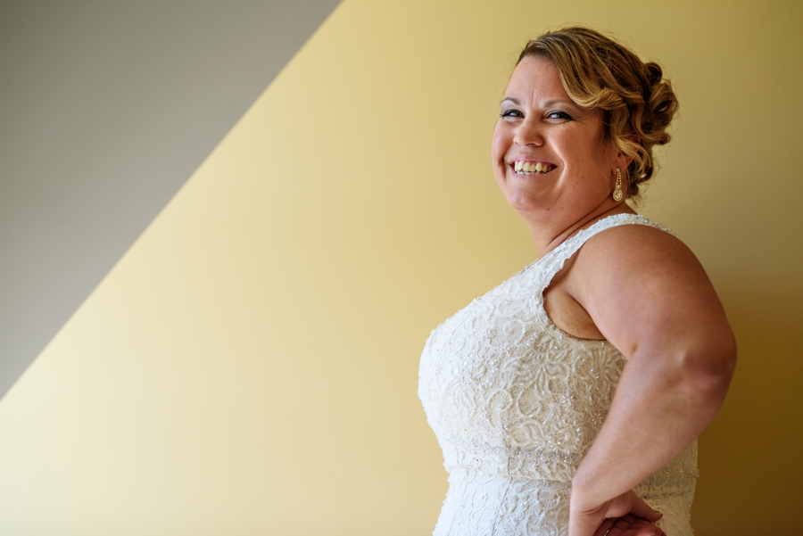 A bride to be in her wedding dress standing in front of a window.